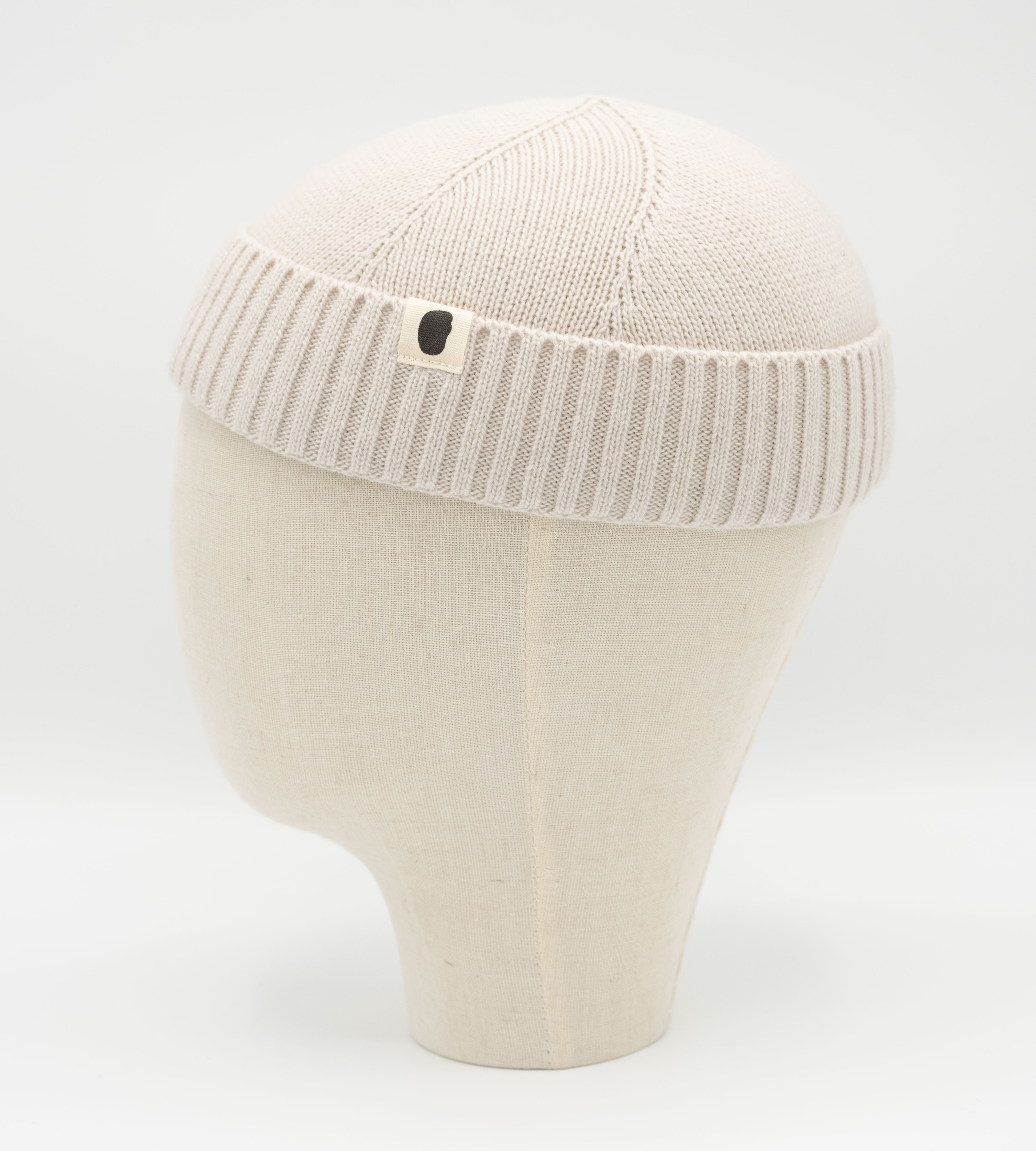 Cremefarbene gestrickte Dockermütze auf Leinenkopfmodell mit kleinem Logo-Etikett