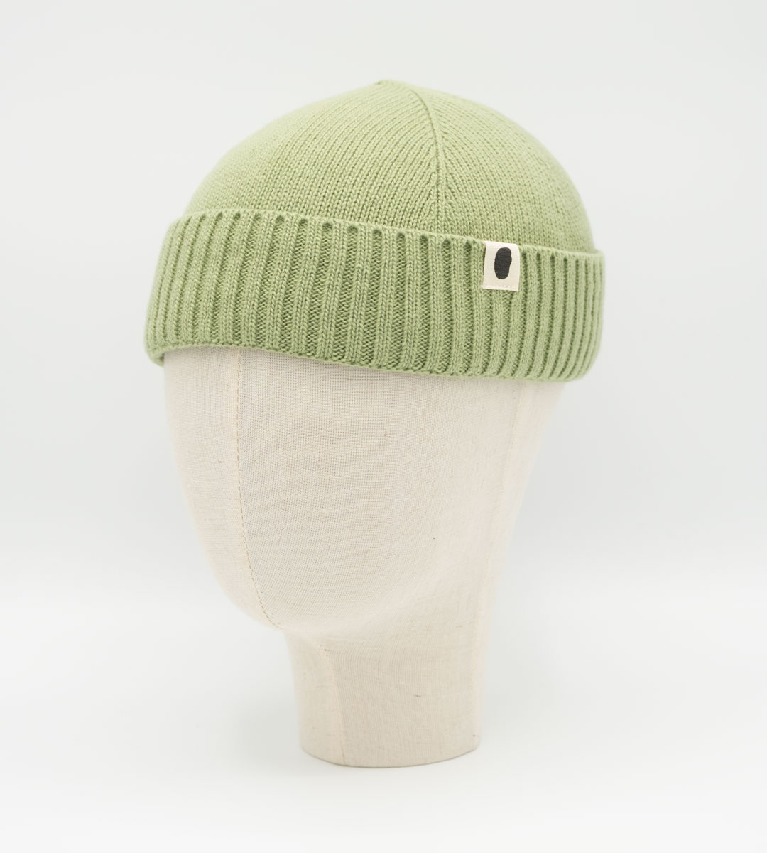 Salbeigrüne Strickmütze mit Rippbund und Logo-Patch auf Leinenkopf-Display
