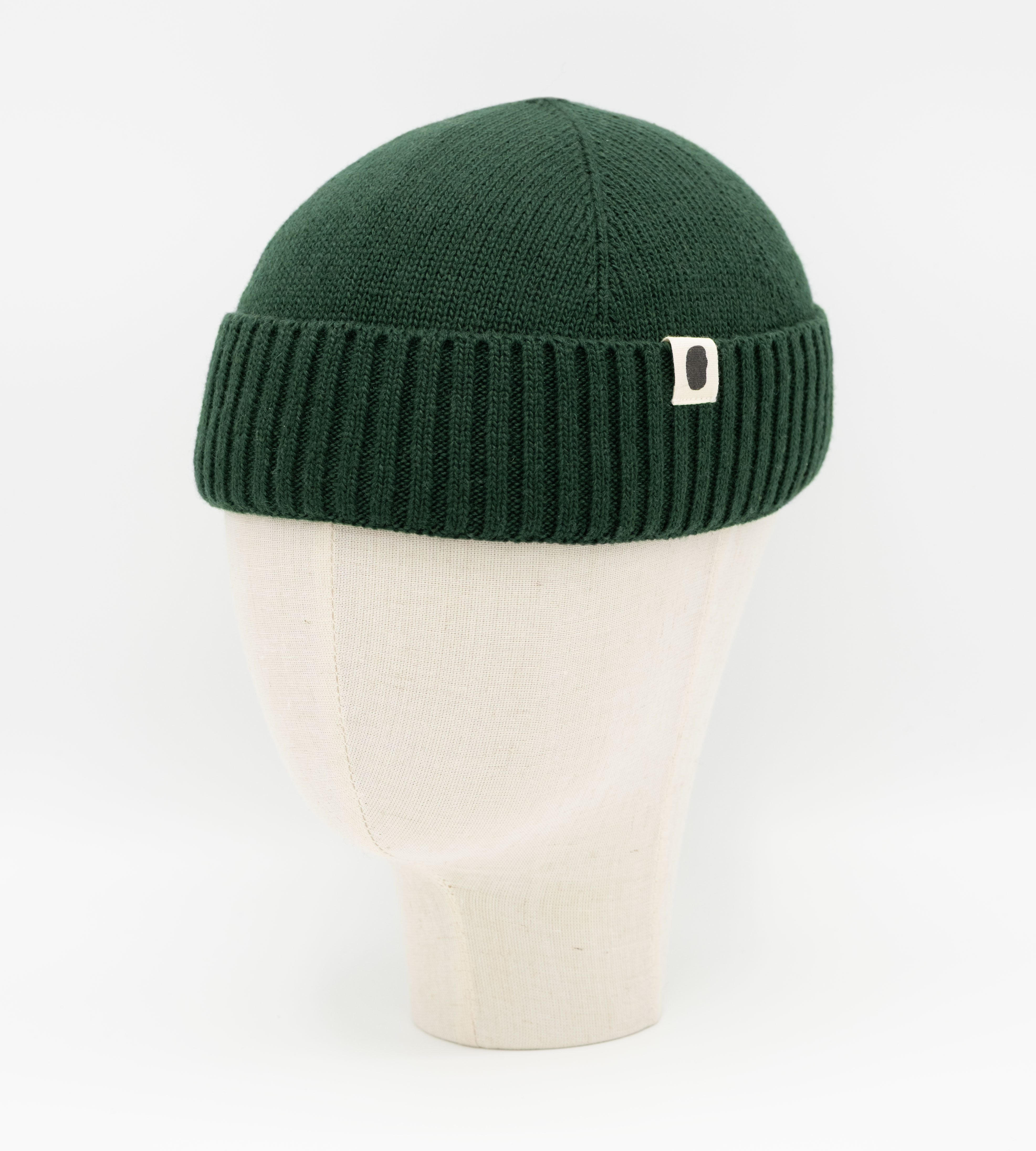 Dunkelgrüne Strick-Beanie mit Rippbund und Logo-Label auf Mannequinkopf