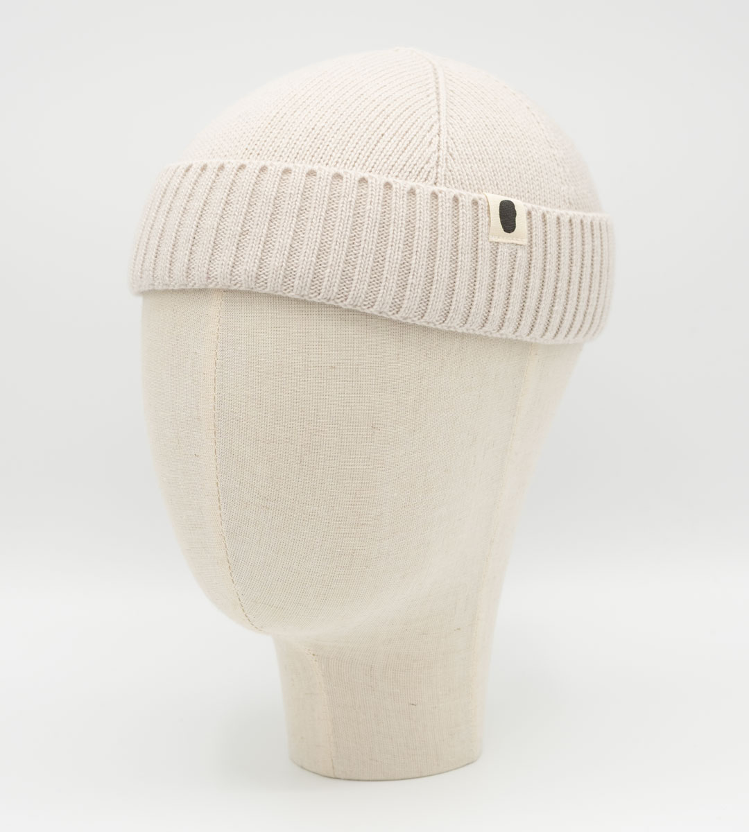 Cremefarbene Strickmütze mit Rippbund und kleinem Logo auf Mannequinkopf